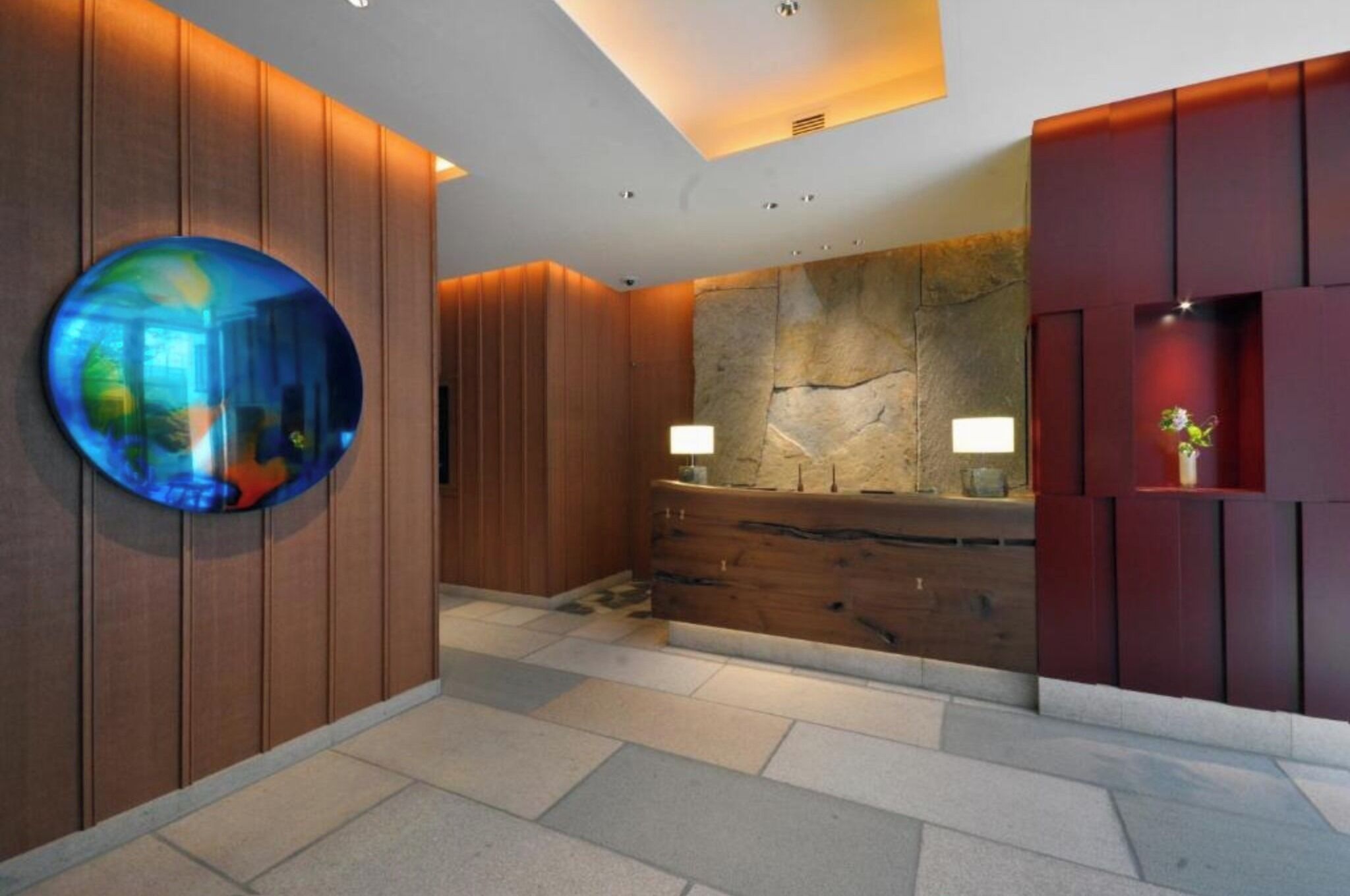 A modern lobby with a stone wall, wooden paneling, a round mirror, and a reception desk.