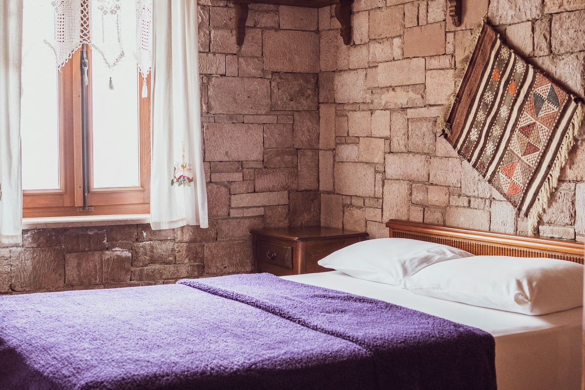 A room with a bed, a nightstand, a window with curtains, and a wall with a patterned tapestry.