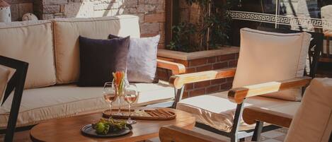 A cozy outdoor seating area with a wooden table, cushioned chairs, and a brick wall backdrop.