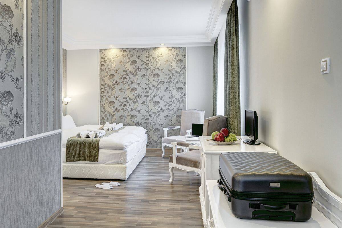 Una habitación de hotel con cama, escritorio, computadora, televisor y maleta.