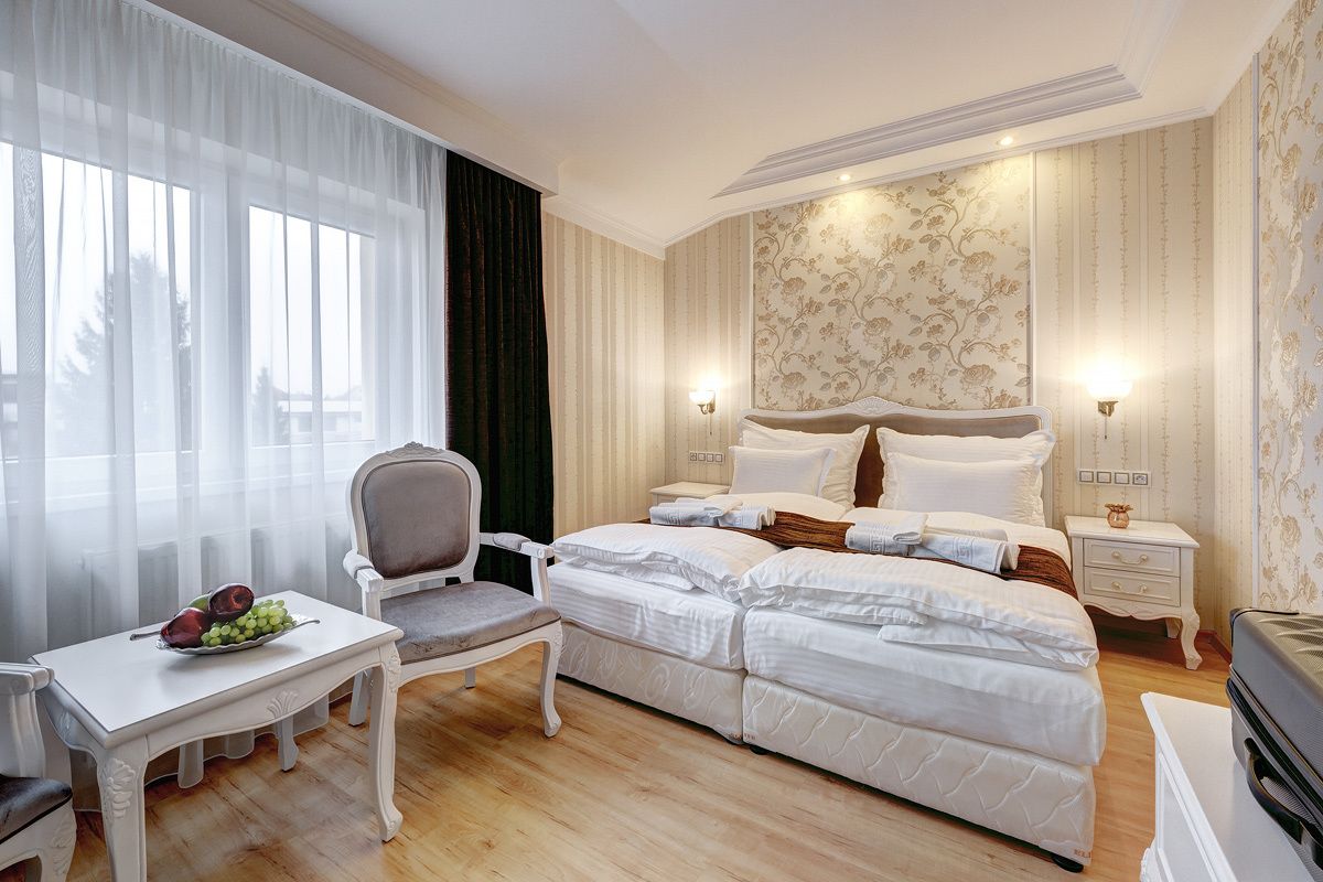 A hotel room with a large bed, a bedside table with a fruit bowl, a chair, and a nightstand with a lamp.