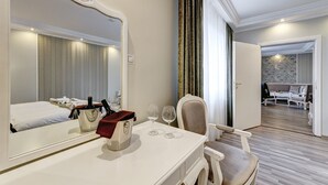 Quarto de hotel com um espelho grande, uma mesa de cabeceira com uma bolsa vermelha, dois copos de vinho e uma cadeira.