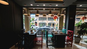 An indoor dining area with tables and chairs, a view of the street outside, and hanging lights. - Minatale Phuket (Patong)