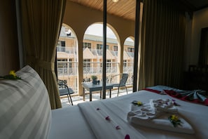Ein Hotelzimmer mit Balkon, einem Bett mit Handtüchern und Blumen sowie Blick auf die Balkone des Gebäudes.