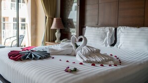A neatly made bed with white linens, a heart-shaped towel arrangement, and rose petals scattered on the bed. - Minatale Phuket (Patong)