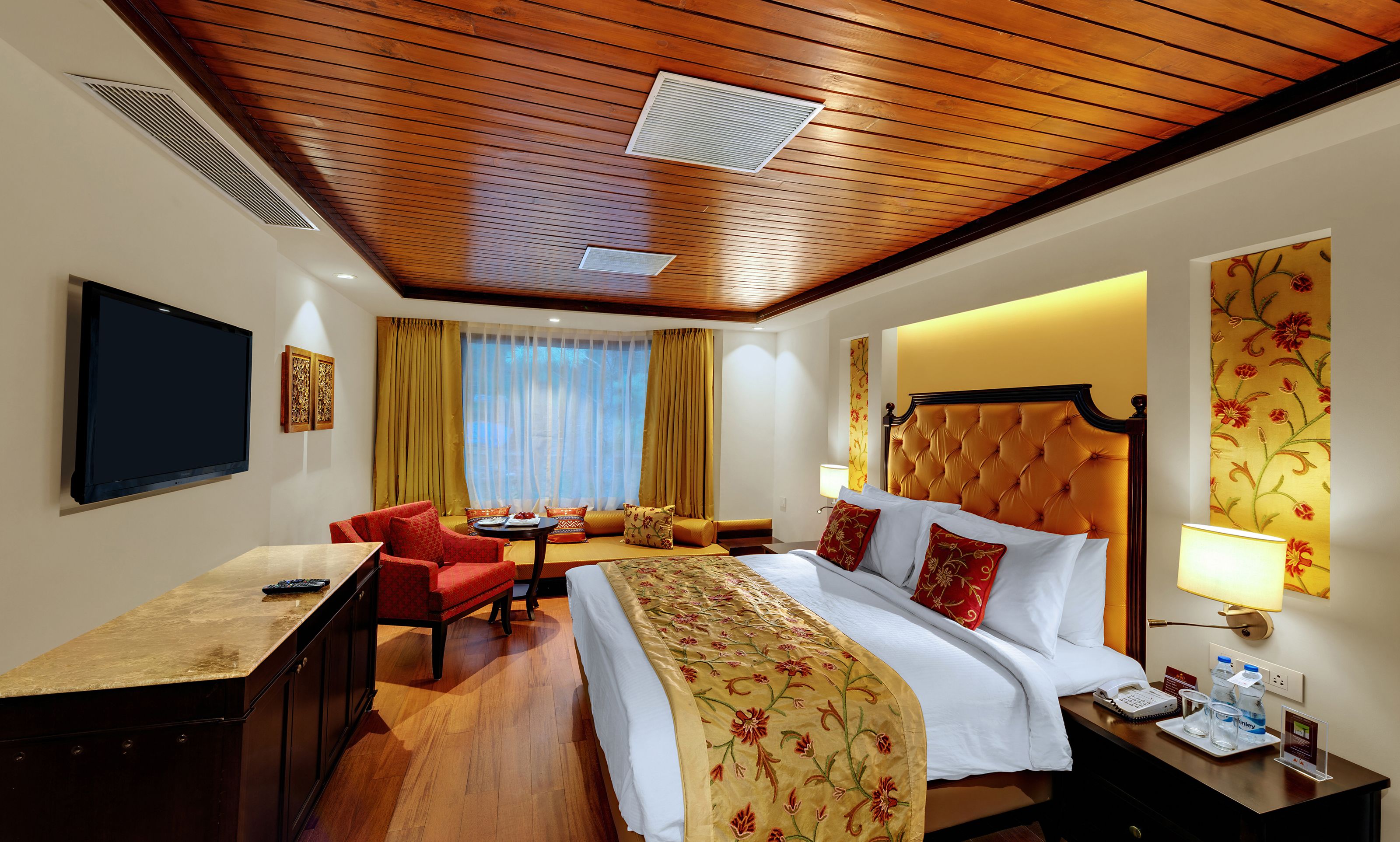 Una habitación de hotel con cama, escritorio, silla, televisor y ventana con cortinas.