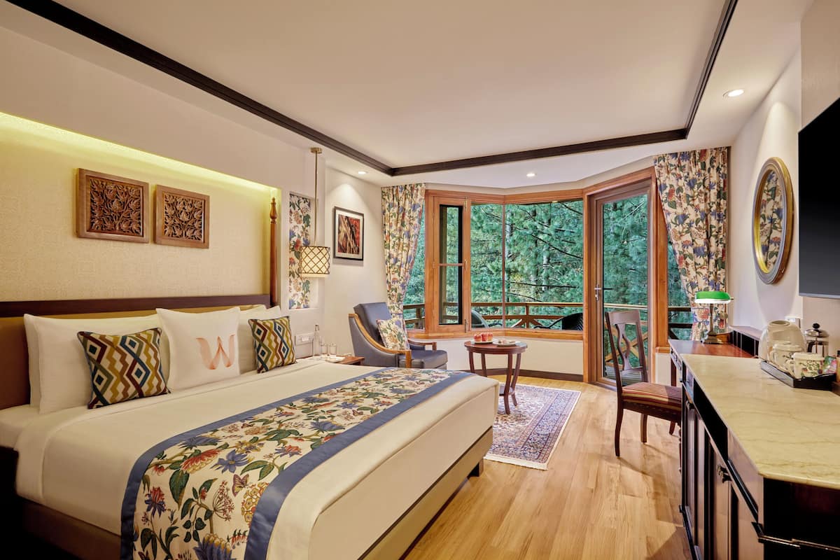 A spacious bedroom with a large bed, a desk, and a view of trees through a large window.
