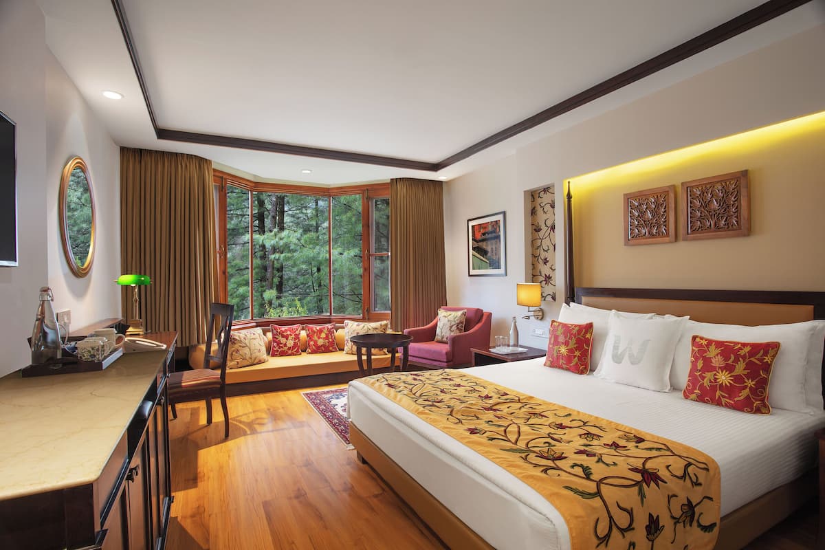 A hotel room with a large bed, a desk, a chair, and a window with a view of trees.