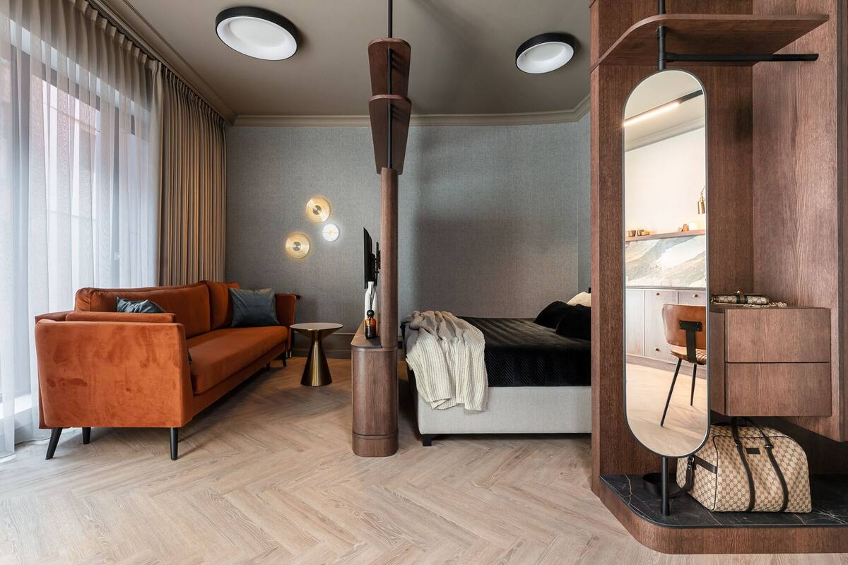 A modern living room with a sofa, a coffee table, a TV, and a bed. There are three pendant lights and a large mirror above the bed.