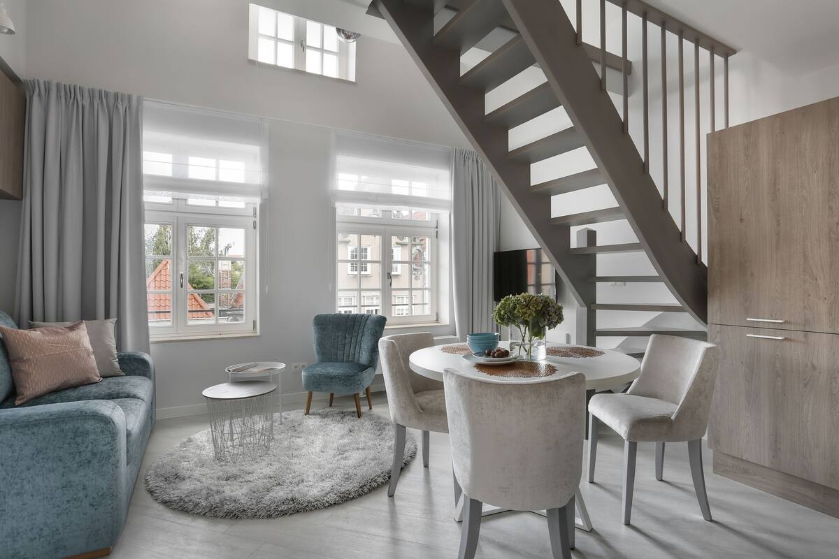 A modern living room with a staircase, a dining area with a round table, and a sofa with a fluffy rug.