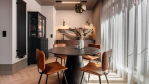 Un espace repas moderne avec une table ronde, des chaises en cuir, un vase contenant des fleurs séchées et, au fond, une cuisine.