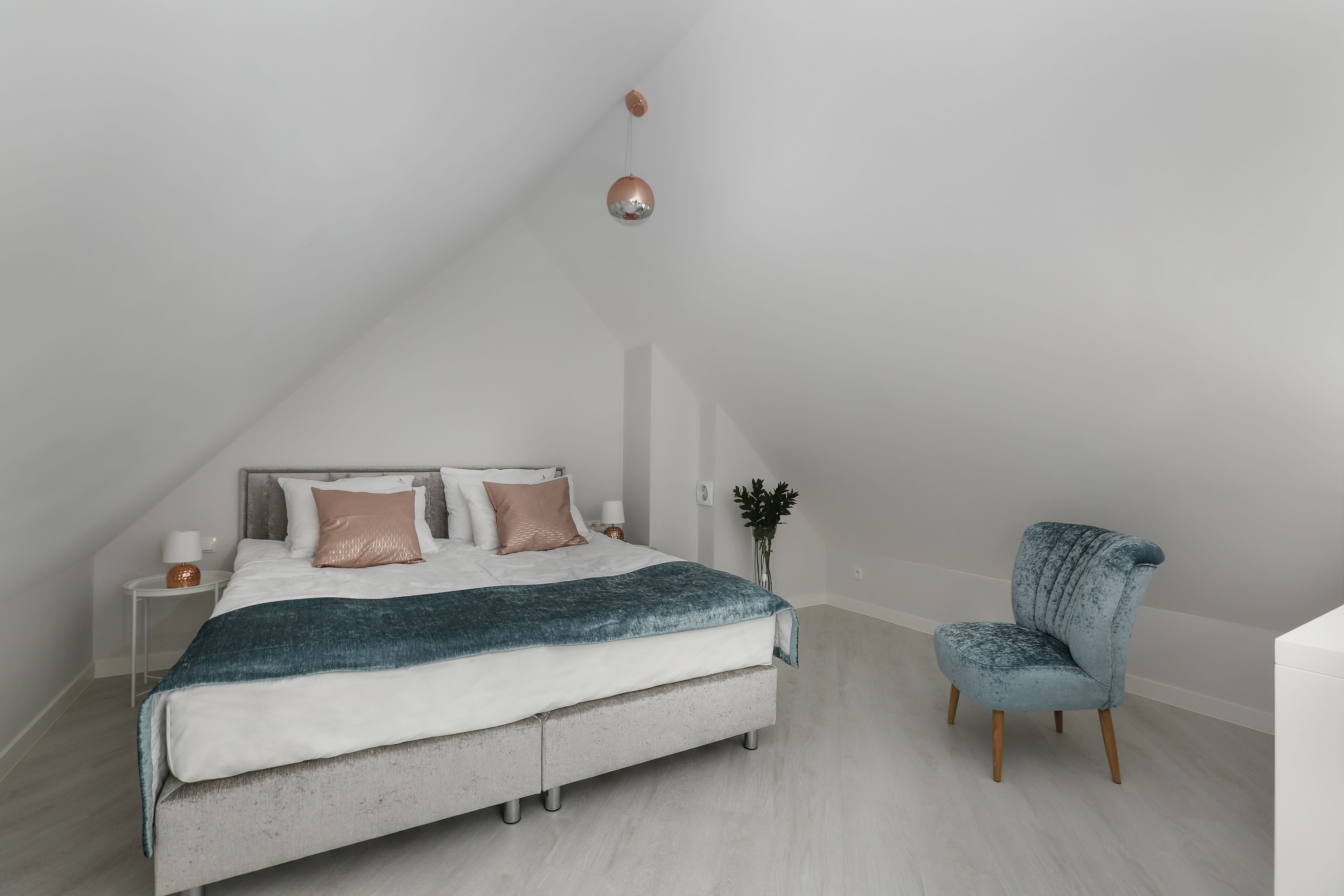 A bedroom with a bed, bedside table, chair, and a hanging light fixture.