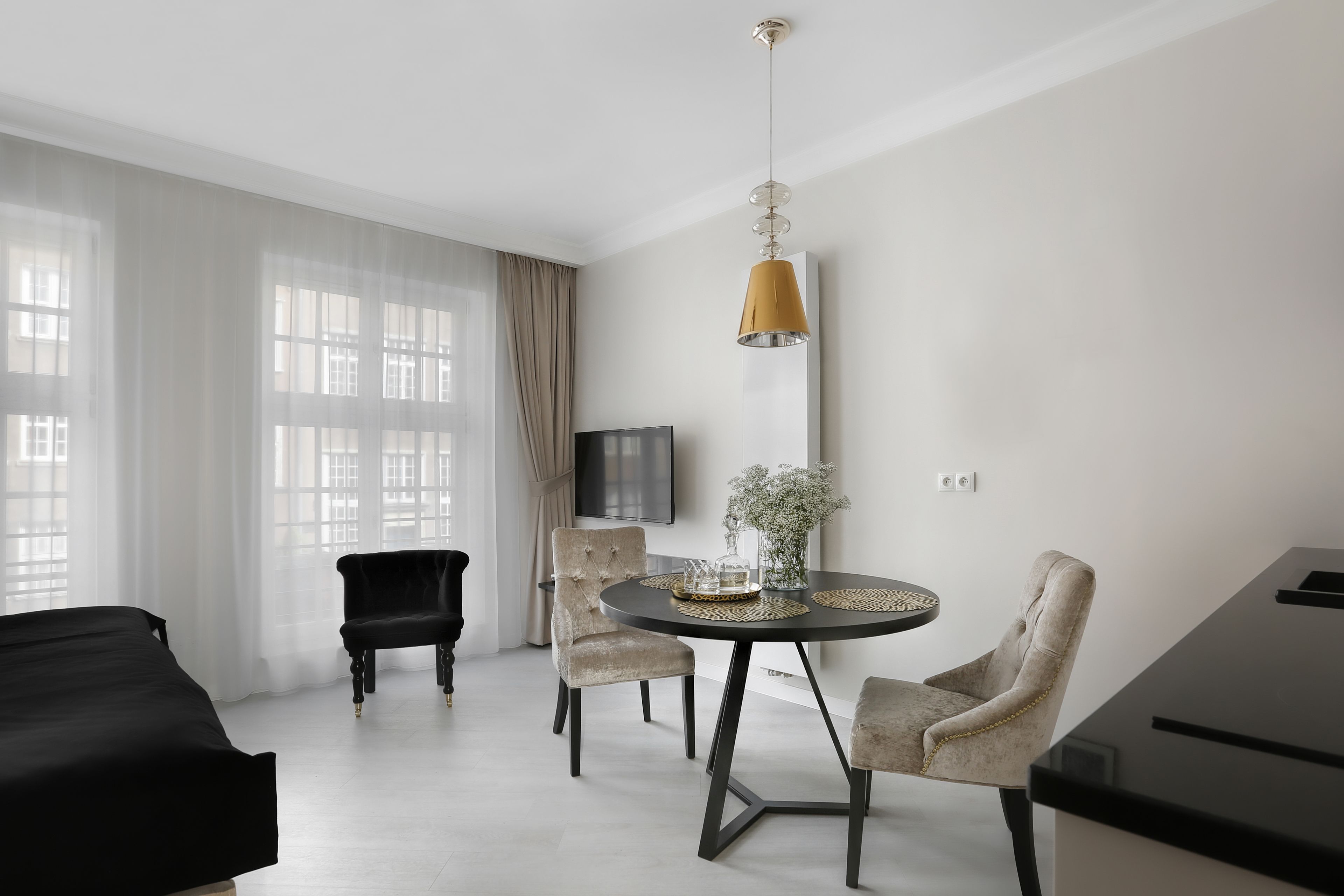 A modern living room with a black sofa, a dining table with two chairs, a piano, and a large window with sheer curtains.
