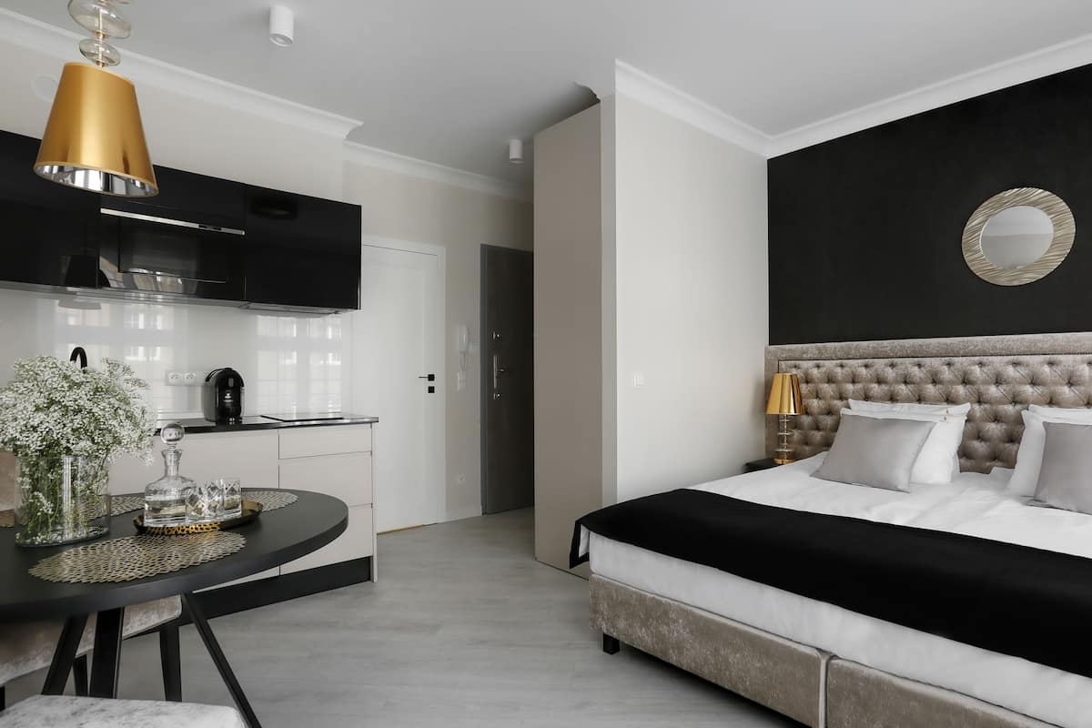 A modern bedroom with a tufted headboard, a round mirror, and a dining area with a table and chairs.