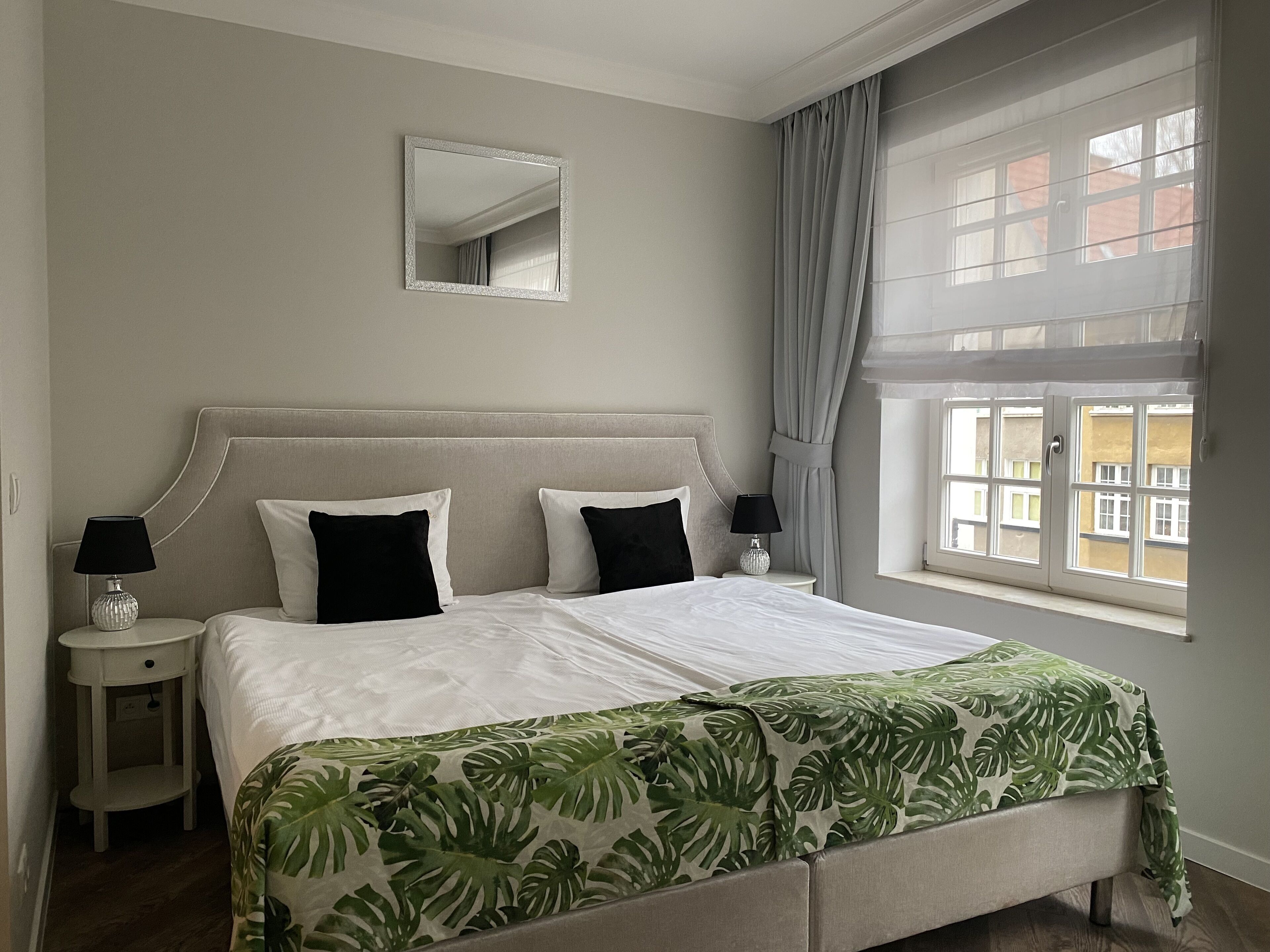 Un dormitorio con una cama grande, dos mesitas de noche, un espejo y una ventana con cortinas.
