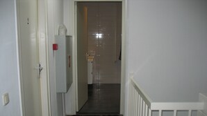 A narrow hallway with a white door on the left, a white railing on the right, and a black doormat at the entrance. - Guest House Amsterdam - Hostel (Amsterdam)