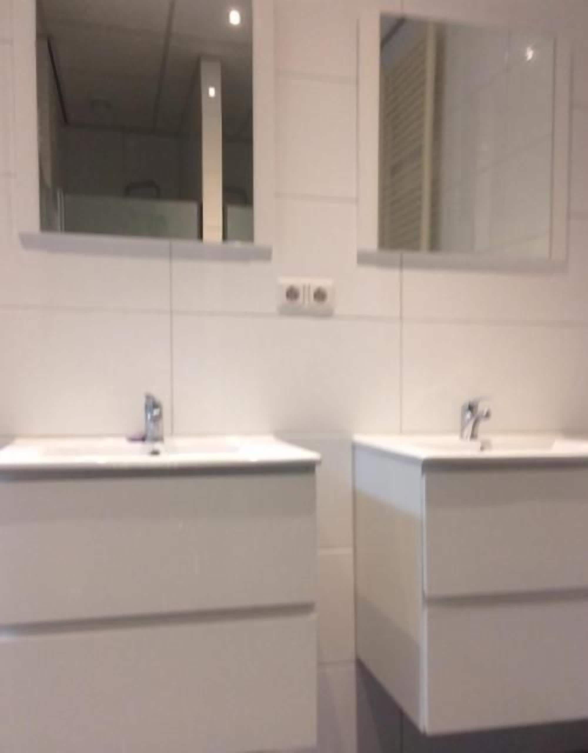 Un baño con dos lavamanos, cada uno con un espejo encima. Debajo de los lavamanos hay dos armarios.