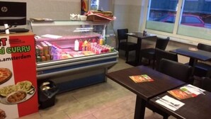 A restaurant interior with a food display case, tables, chairs, and a menu stand. - Guest House Amsterdam - Hostel (Amsterdam)
