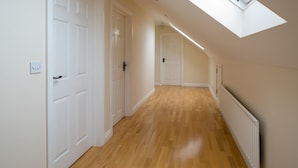 A corridor with wooden flooring, white doors, and a skylight.