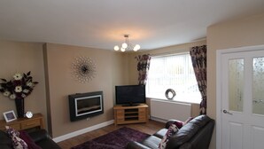 A living room with a fireplace, television, and a door. - Colliery Cottage (Durham)