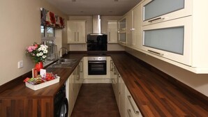 A modern kitchen with wooden countertops, stainless steel appliances, and white cabinetry. - Colliery Cottage (Durham)