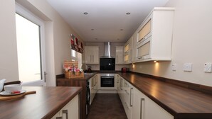 A modern kitchen with wooden countertops, stainless steel appliances, and white cabinetry. - Colliery Cottage (Durham)