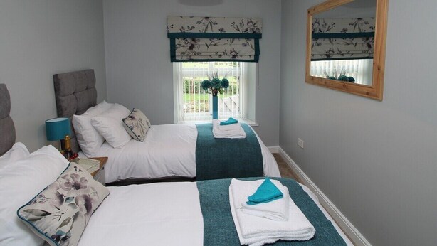 A hotel room with two beds, a large mirror, a window with a view of the outdoors, and a ceiling light fixture. - Colliery Cottage (Durham)