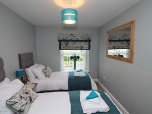 A hotel room with two beds, a large mirror, a window with a view of the outdoors, and a ceiling light fixture. - Colliery Cottage (Durham)
