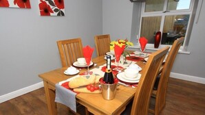A wooden dining table set for six with red napkins, white plates, and a bottle of champagne. - Colliery Cottage (Durham)