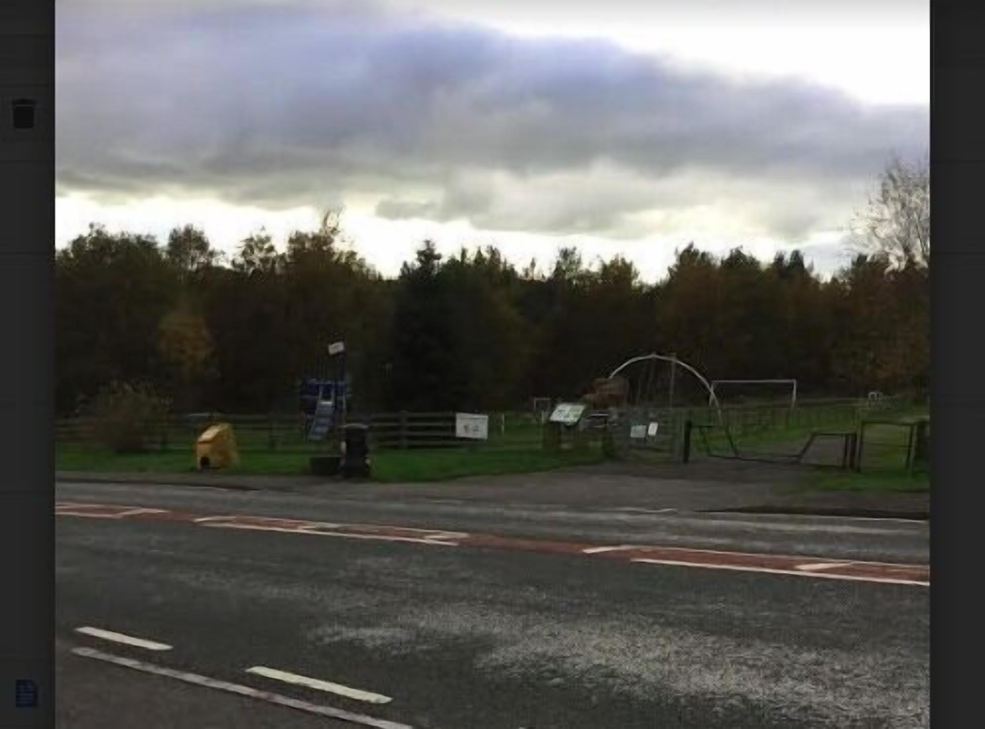 A road with a pedestrian crossing and a fenced area with a playground.