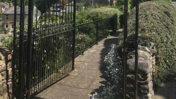 Une entrée fermée par un portail, avec un chemin de pierre menant à un bâtiment doté d’une tour.