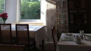 Une salle à manger agrémentée d’un lustre, une table dressée pour deux personnes et une vue sur la verdure à l’extérieur.