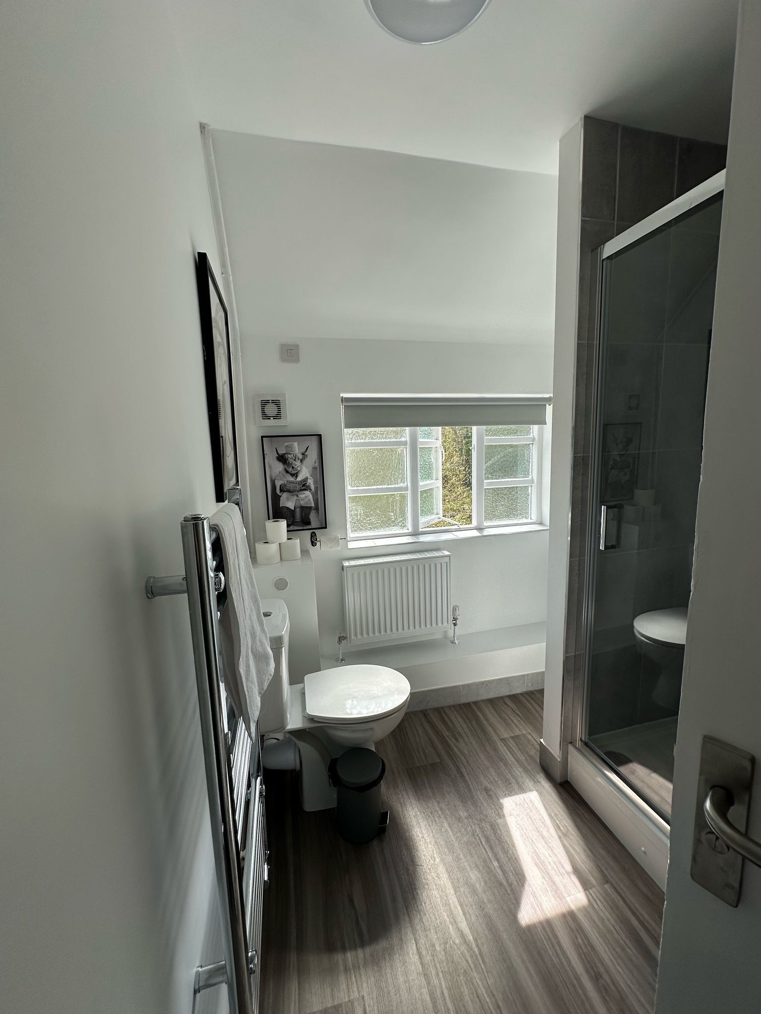 A modern bathroom with a toilet, bidet, and shower. It features a window providing natural light and a view of greenery outside.