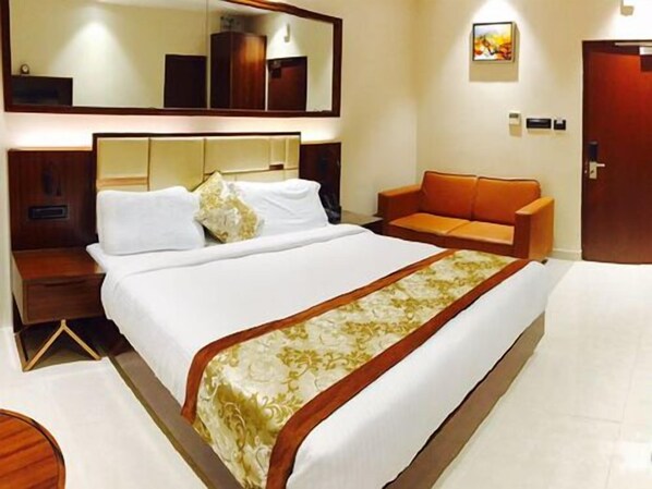 Une chambre d’hôtel avec un grand lit, une table de chevet en bois, un canapé, un miroir et une porte.