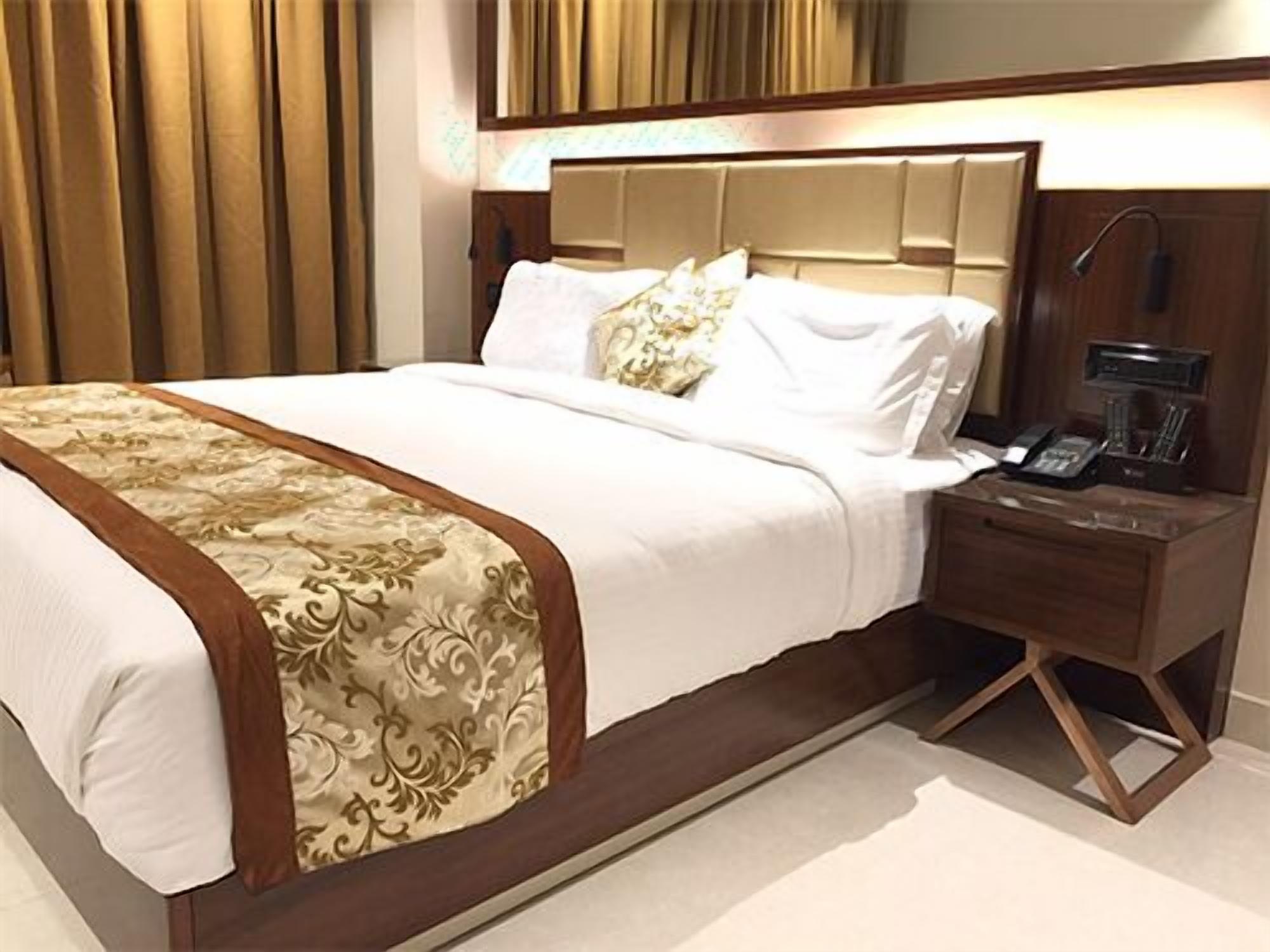 A hotel room with a large bed, a wooden nightstand, a coffee maker, and a lamp.