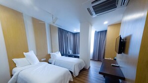 A hotel room with two beds, a desk, a TV, and an air conditioning unit. - Vybrant Hotels (Vijayawada)
