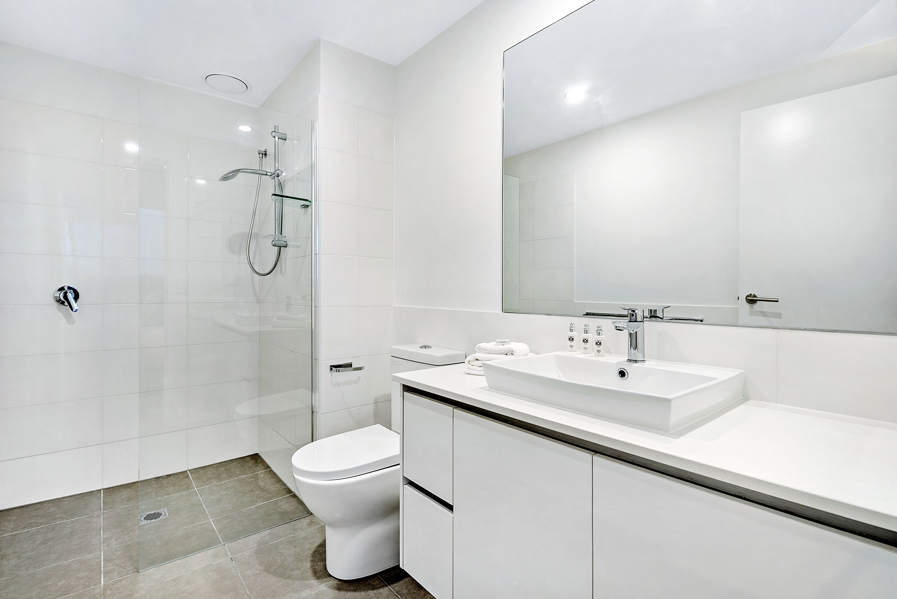 A modern bathroom with a glass-enclosed shower, a white toilet, and a large mirror above a white sink.