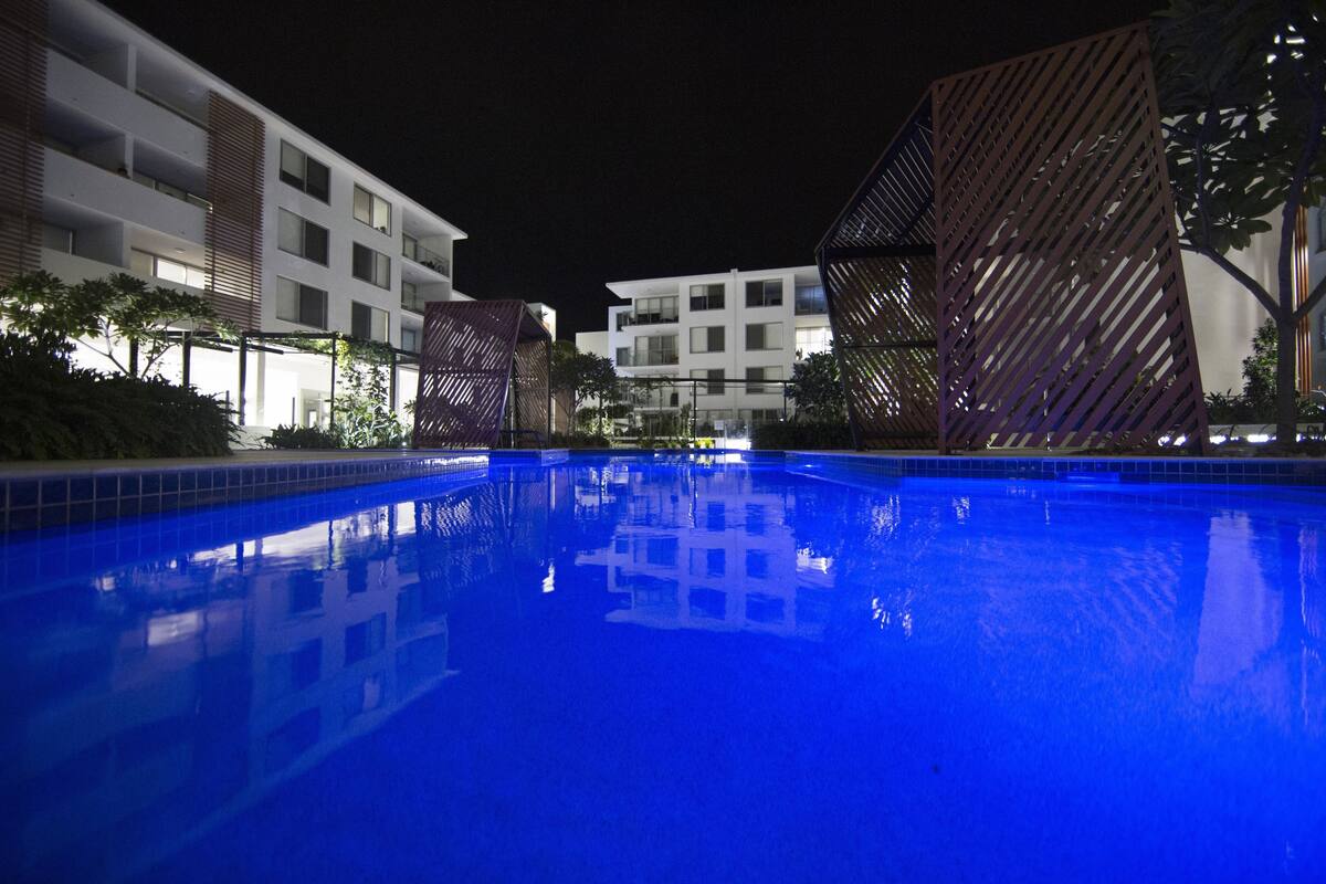 Una piscina nocturna con reflejos de edificios y árboles.