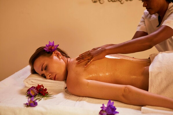 A person receiving a back massage in a room with a white bed and a wall with text.