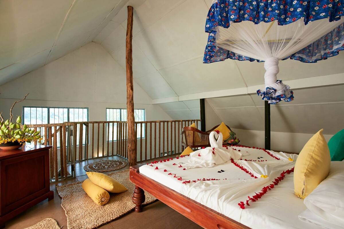 Een slaapkamer met een bed, een houten hoofdbord, een hangende hemel, een potplant en een balkon met een hek.