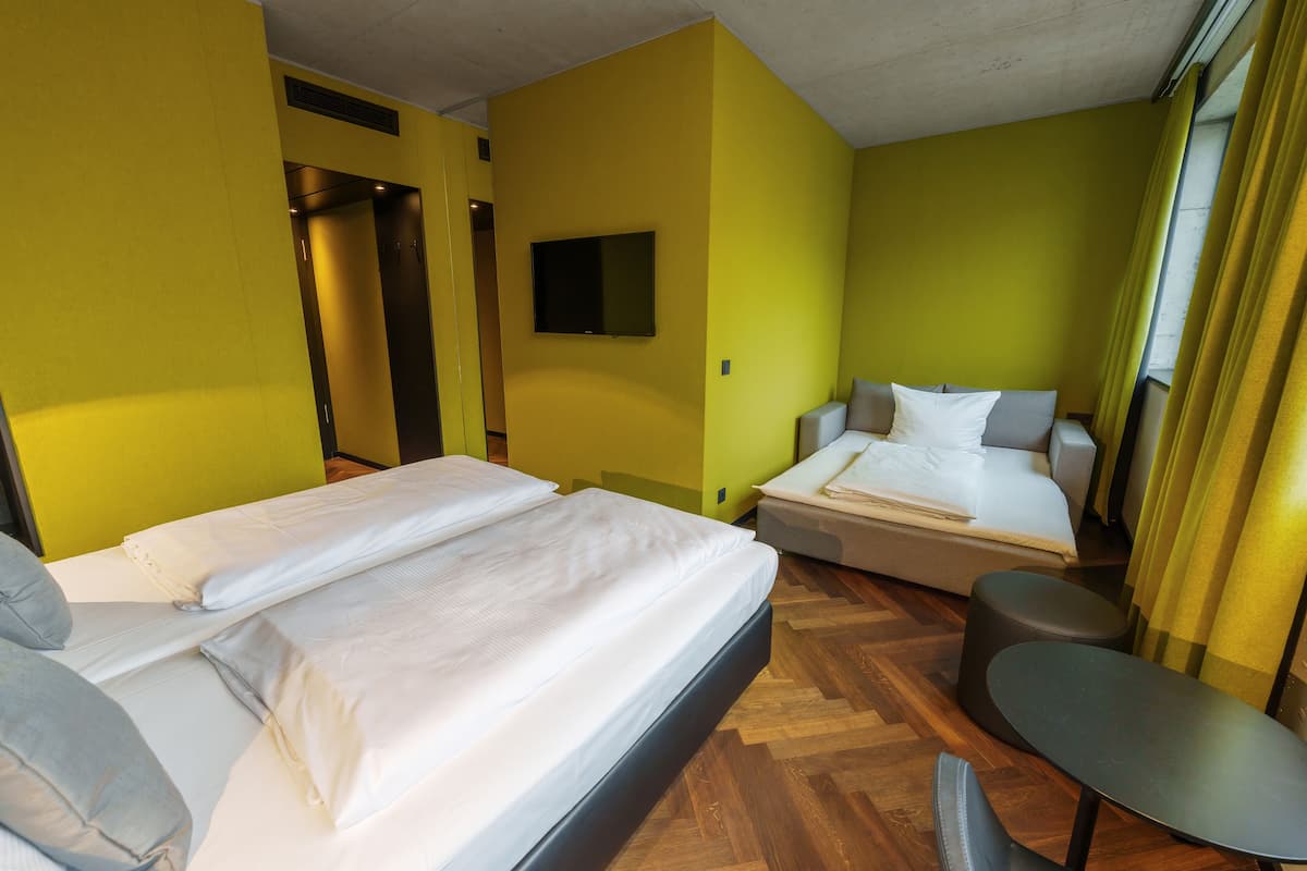 A hotel room with two beds, a small table, and a TV on the wall.