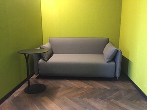 A small, enclosed room with a grey sofa and a small round table. The walls are painted green, and the floor has a herringbone pattern. - Roomreich (Ingolstadt)