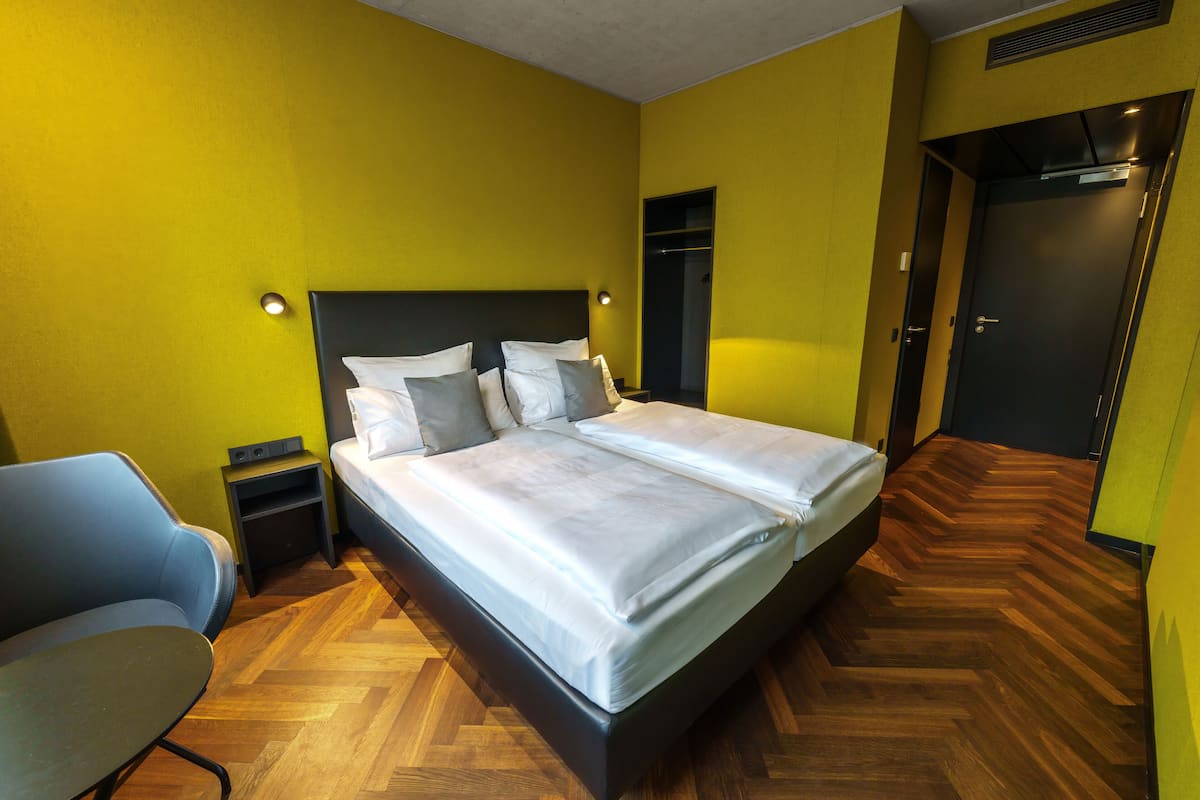 A double bed with a black frame, two bedside tables, a chair, and a wardrobe.