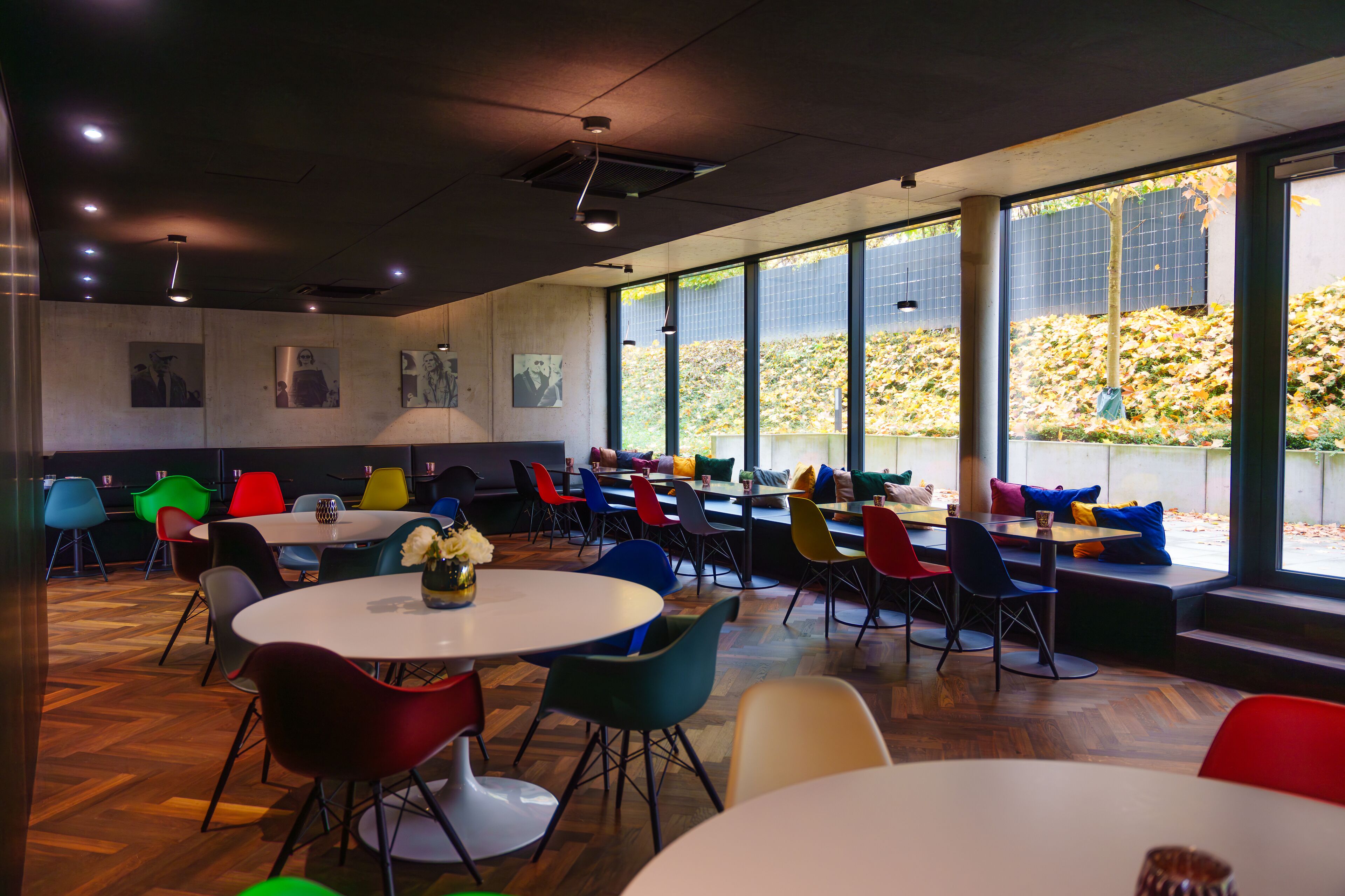 A modern dining area with colorful chairs and tables, large windows with a view of greenery, and artwork on the walls.