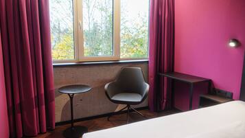 A room with a bed, a chair, a small table, and a window with curtains.