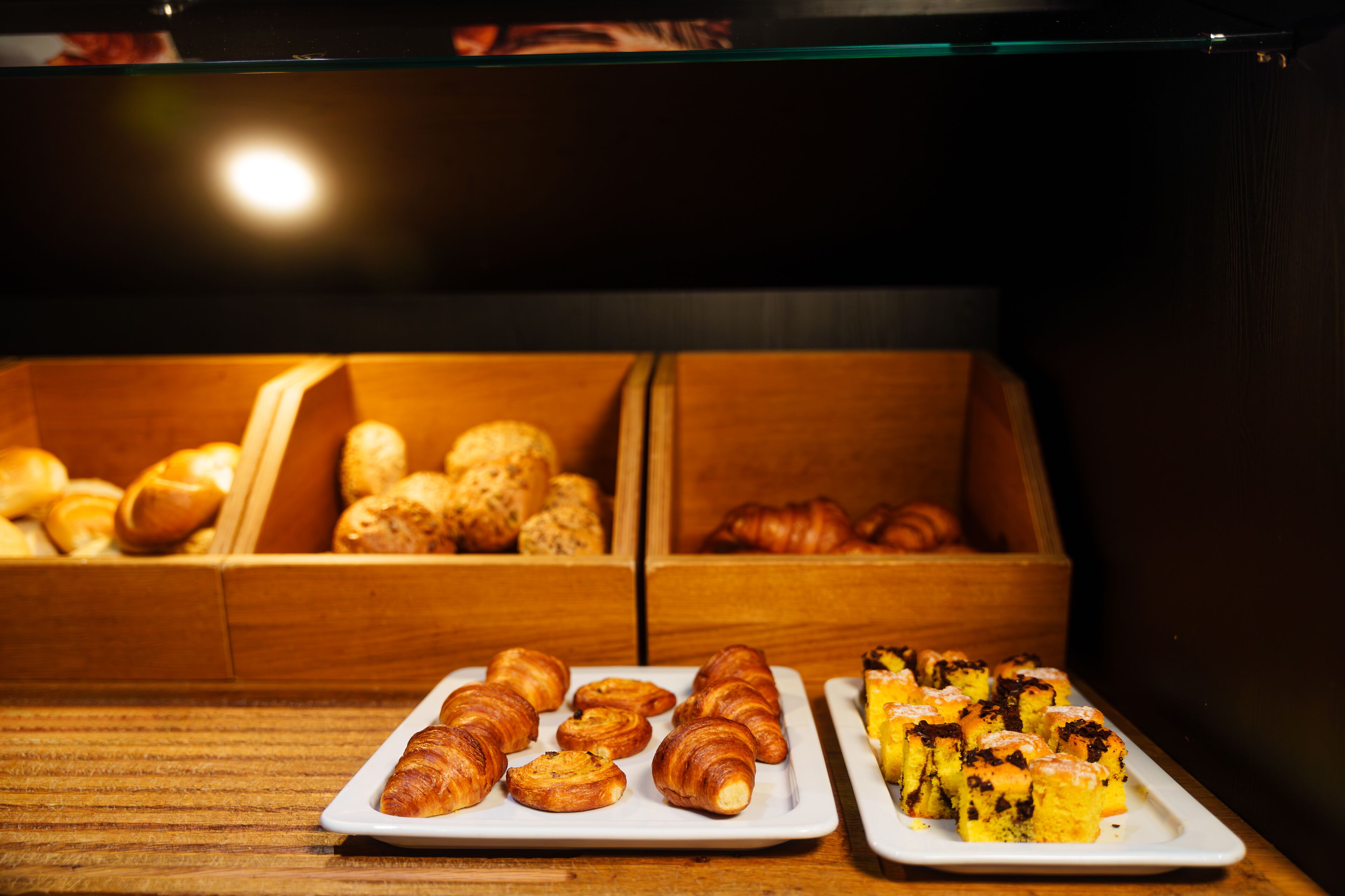 Una exhibición de pasteles en la sección de panadería, con croissants y muffins sobre platos blancos.