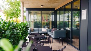 An outdoor seating area with tables and chairs, a sofa, and a glass wall with a sign. - Roomreich (Ingolstadt)