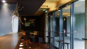 A modern bar area with a wooden floor, bar stools, a large white vase, and a seating area with tables and chairs. - Roomreich (Ingolstadt)