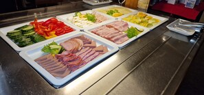 A buffet with various food items including sliced meats, vegetables, and cheese.