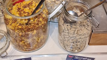 A breakfast buffet with various cereal options in jars, a candle, and a sign indicating 'Muisli' and 'Horefras'.